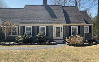 Dark gray painted horizontal vinyl-sided residential home with white-trimmed multi-pane windows and brick chimney in Cape