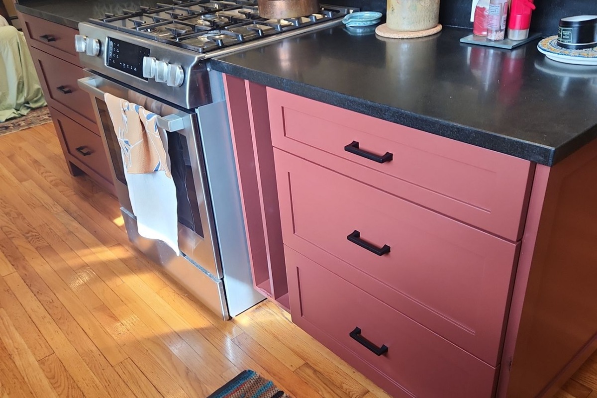 Modern Kitchen Cabinet Painting with Custom Terracotta Finish Newly painted terracotta kitchen cabinets and drawers with black countertops and a stainless steel range.