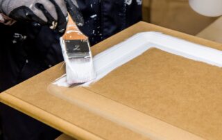 A professional painter applies a fresh coat of white paint to a kitchen cabinet door with a brush. This is for a homeowner who knew when to replace kitchen cabinets.