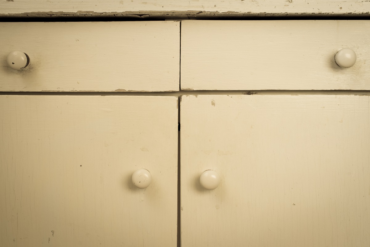 Worn Kitchen Cabinets Needing Professional Painting Service Close up of old, chipped, and peeling off white kitchen cabinets and drawers with round knobs.
