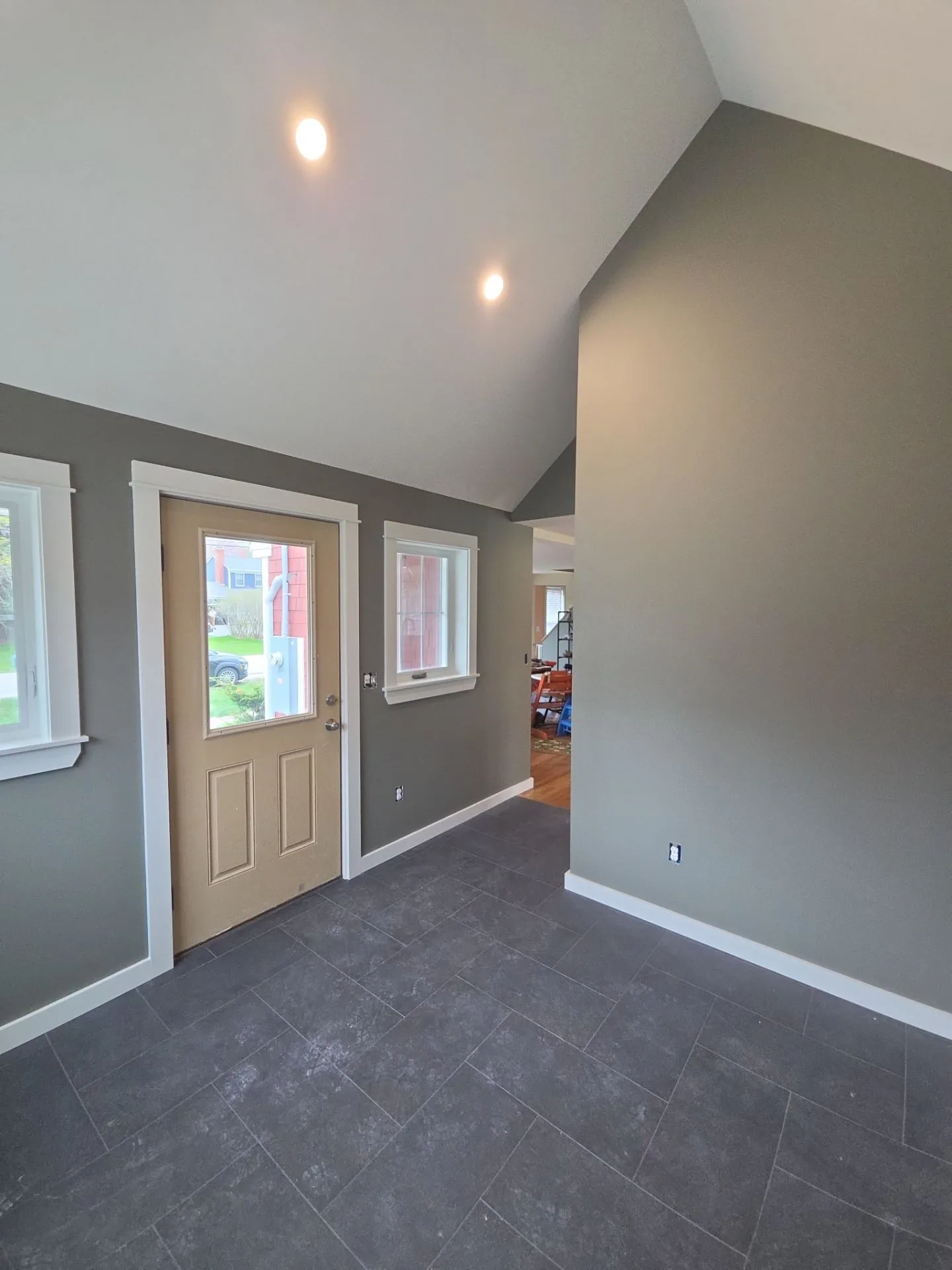 Charcoal Gray Entryway with White Trim Charcoal-gray painted entryway with white trim, vaulted ceiling, recessed lights, tan door, and slate tile flooring.